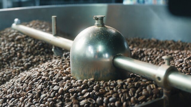 Close up coffee beans rotating through industrial mixer and drum roaster at factory blending brown grains roast production process automatic equipment beverage preparation caffeine manufacturing food
