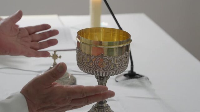 A priest holds up a gold ciborium over the altar during the consecration at Catholic mass, with a cross, candle and open missal beside him.