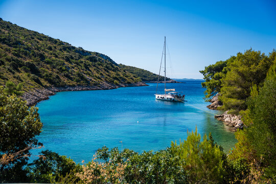 Sailboat anchored in a tranquil bay surrounded by lush green hills and clear blue waters under a bright sunny sky in Solta island, Croatia