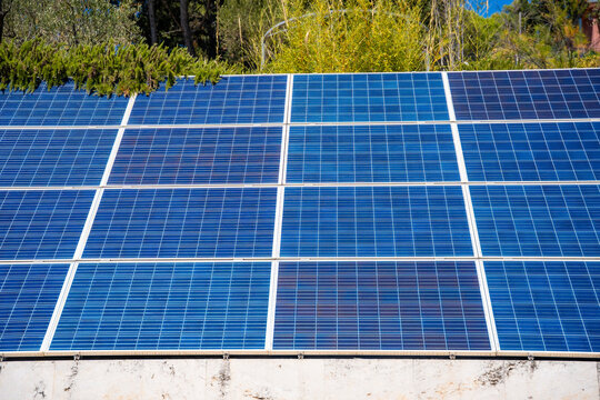 Solar panels installed on a rooftop, showcasing blue photovoltaic cells under bright sunlight with greenery in the background, Croatia