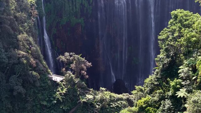 Panoramic canyon waterfall framed by dense rainforest, dramatic cliffs and a small observation platform.