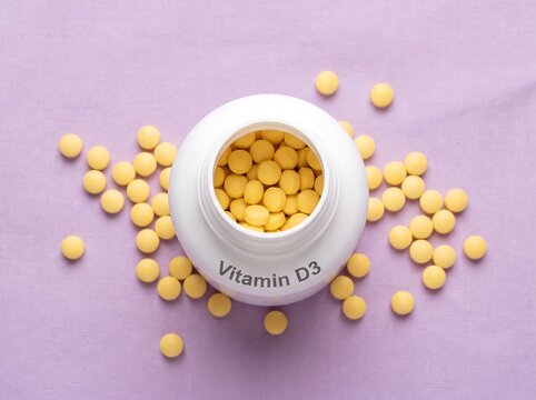 Open white bottle of Vitamin D3 yellow supplement pills scattered on pastel purple background, flat lay overhead view for dietary health, immunity boost, and nutrition concept
