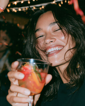 Woman laughing while holding a cocktail at a nighttime party with string lights