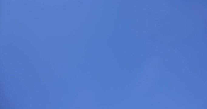 View of a small white drone flying high in mid-air against a blue sky with clouds and mountain peaks