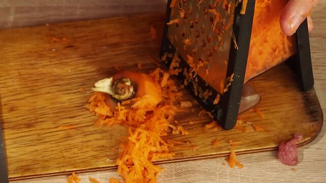Man grates carrot on stainless steel grater