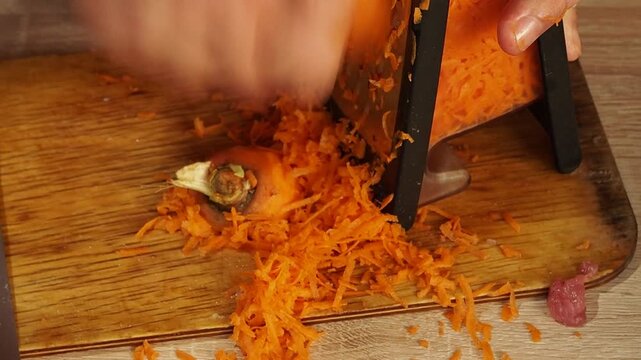 Man grates carrot on stainless steel grater