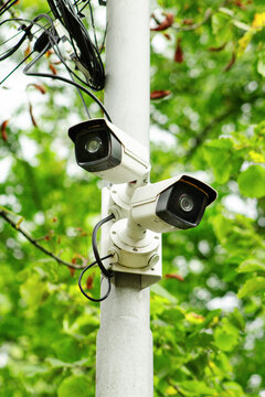 Outdoor security camera. CCTV cameras on pole. Dual surveillance system. White CCTV unit. Security monitoring technology. Public safety camera. Park surveillance setup. Outdoor CCTV equipment. Bullet