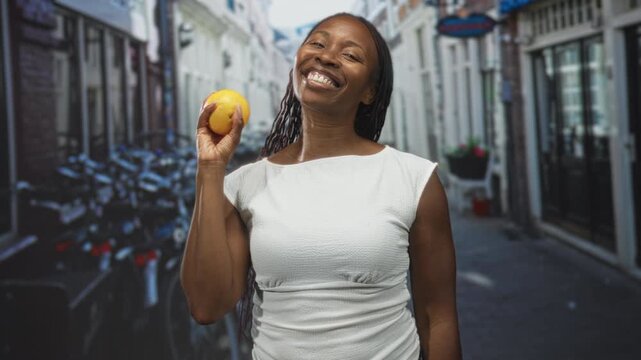 Woman holding lemon in hand on a narrow cobbled street with parked bicycles and storefronts; joy vitality.