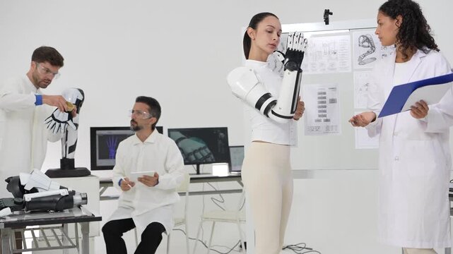 Robotics lab teamwork with a woman in a bionic arm, a scientist at a monitor showing a digital hand scan and an engineer adjusting a robot leg