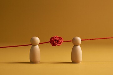Obraz premium Two wooden figures face red knotted string on