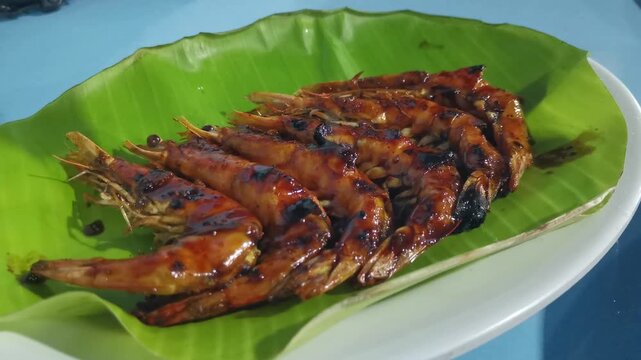 Hand squeezing lime over grilled prawns served on a banana leaf on a white plate