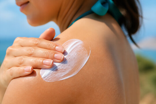 A person is applying a white cream or lotion to their shoulder outdoors on a sunny day.
