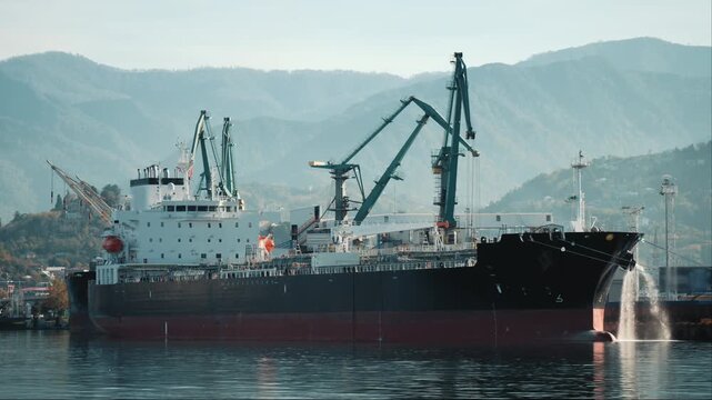 Industrial port tanker framed by cargo cranes and mountains, commercial shipping scene for maritime logistics, freight transport and global supply chain.