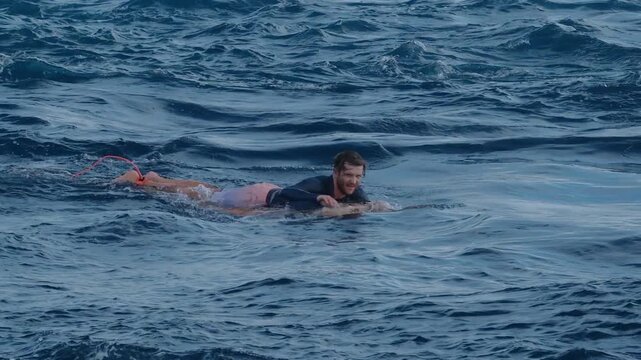 Male surfer paddles against the strong current