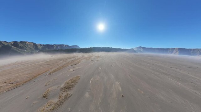 Aerial fisheye drone view of Mount Bromo sand sea with sunlit dust and distant caldera rim