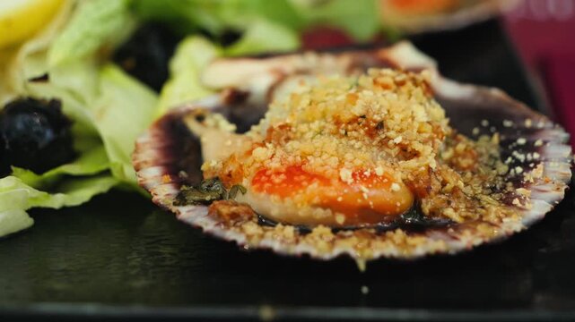 Close-up of a baked scallop served in its shell with golden parmesan crust. Gourmet seafood appetizer presented in a restaurant, Mediterranean cuisine and fine dining concept.