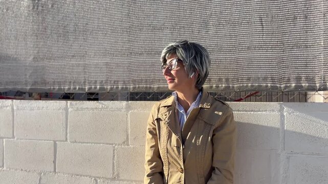 Mujer +50 esperando el autob&uacute;s junto a una pared urbana