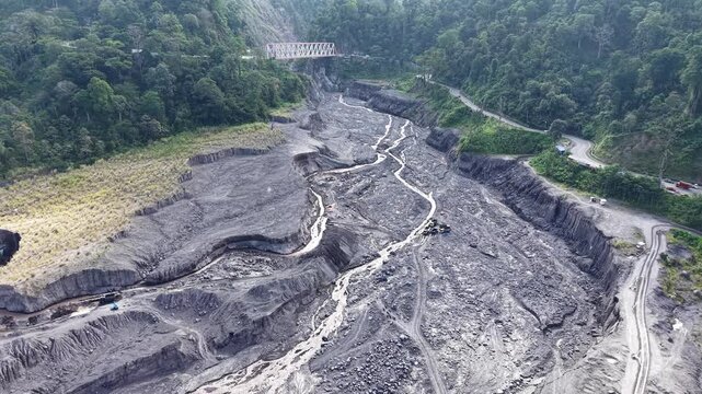 Aerial view looking down at a large scale sand quarry operation operating on a dark volcanic sediment plain of Mount Semeru