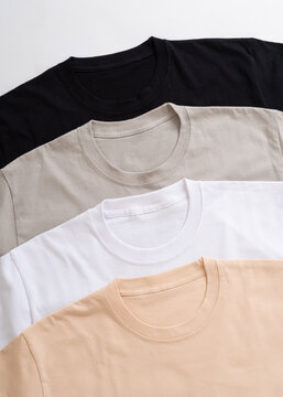 Collection of blank basic t-shirts in black grey white and beige arranged neatly on a plain background for fashion mockup