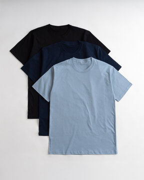 Three blank cotton tshirts in light blue navy and black colors stacked on a white background