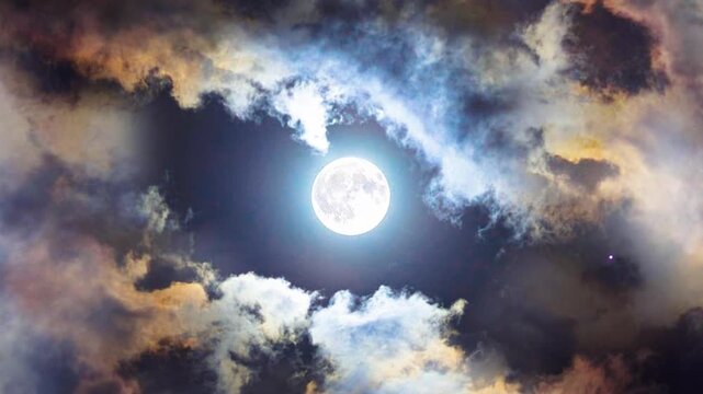 View of the full moon shining brightly among the dramatic clouds in the night sky.