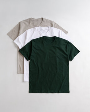 Three plain cotton t-shirts in dark green white and light grey stacked on a white background