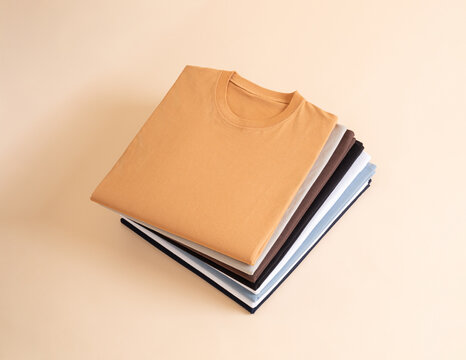 A stack of neatly folded colorful cotton t-shirts displayed on a light beige background