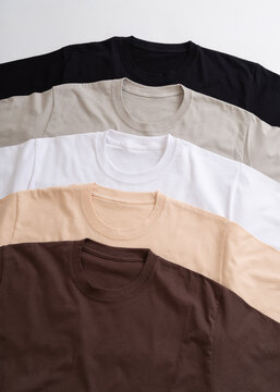 A collection of plain round neck t-shirts in various neutral earth tones stacked neatly
