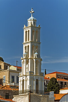 A blue dome and white cross of Church of Agios Nikolaos rise above the ornate Halki tower, with a lone gull perched on the ledge under clear island sky.