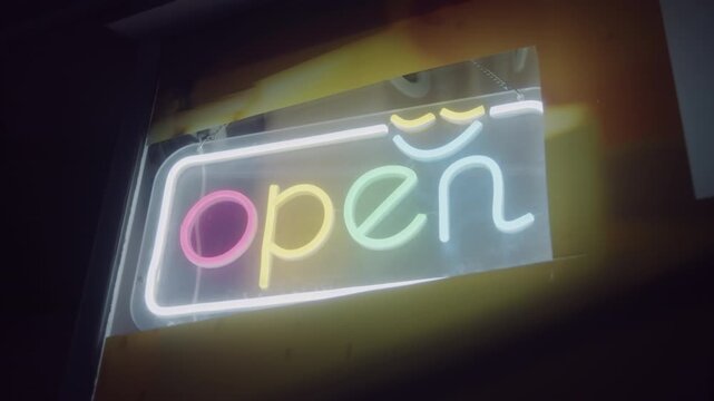 Colorful neon-style LED sign spelling open glows in a shop window at night, warm cinematic shot for small business promos, cafe and retail marketing or social media ads.