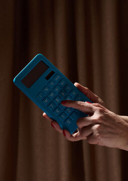 A person calculating on a blue calculator against a dark background.