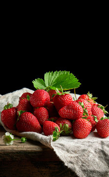 Ripe juicy strawberries with leaves on a linen napkin and wooden table