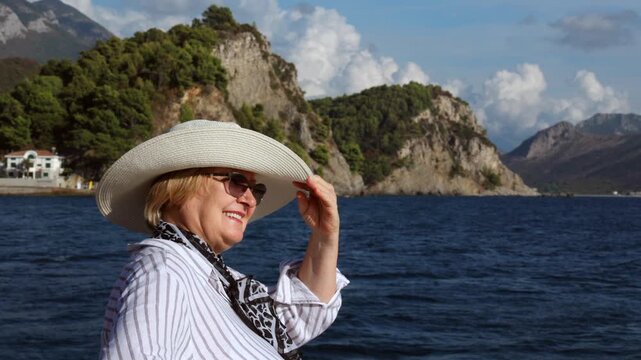 Smiling senior woman enjoying retirement travel and a relaxing seaside vacation with scenic mountains in the background.