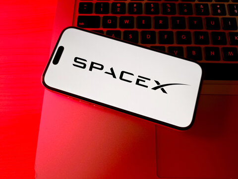SpaceX logo displayed on smartphone screen on laptop keyboard under red lighting