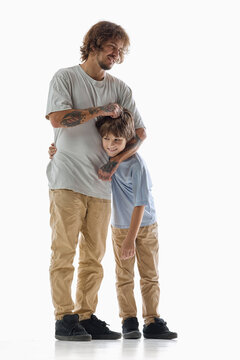 Caring father embraces son and gently pats his head on white studio background. Parental affection, protection and emotional security concept.