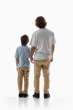 Father and son stand side by side with backs to camera on white studio background. Family unity, generational connection and shared future concept.