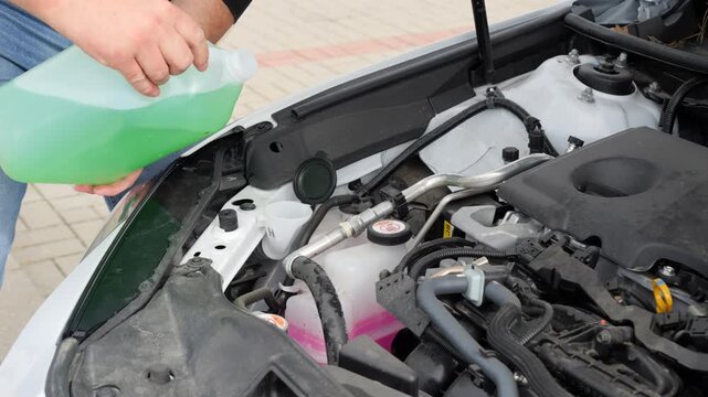 Driver pours windshield washer fluid into the reservoir during routine vehicle maintenance