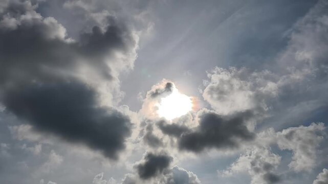 A dynamic sky filled with clouds of varying densities, illuminated by sunlight breaking through with radiant rays. 