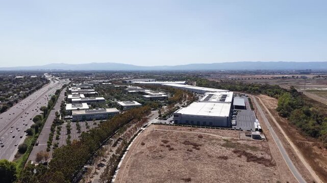 Aerial perspective slowly panning over a corporate office park and a large distribution warehouse center located next to a busy freeway in Silicon Valley on a sunny day