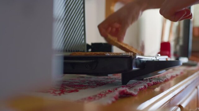 Toast sandwich breakfast kitchen grill static close up of a hand preparing hot toasted bread on an electric maker. Healthy morning food preparation.