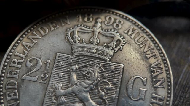 Macro detail video of an antique 1898 Dutch 2.5 gulden pattern coin, highlighting the crowned heraldic design, engraved denomination, and distinctive historical numismatic craftsmanship.