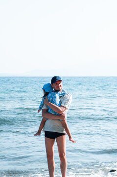 Father Carrying His Little Daughter in His Arms on a Sunny Beach