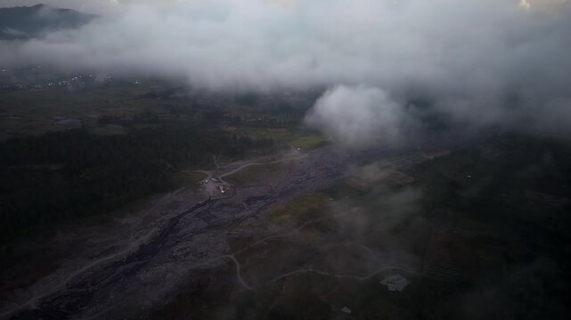 Drone aerial over foggy rural valley with riverbed and scattered village lights at dawn at Pronojiwo, East Java, Indonesia