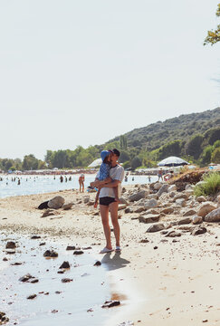 Father Carrying His Little Daughter in His Arms on a Sunny Beach