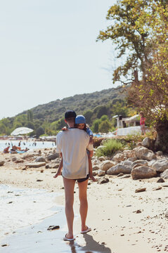 Father Carrying His Little Daughter in His Arms on a Sunny Beach