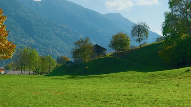 Alpine meadow mountain barn hillside background with green grass and majestic peaks, handheld panning shot. Scenic rural landscape in the European Alps during a bright sunny day.