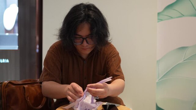 A seated man looks down while handling small items taken from a translucent drawstring pouch.