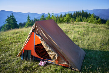 Orange tourist tent in lush green meadow with mountains in background. © anatoliy_gleb