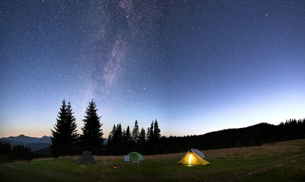 Several tents on grassy clearing under breathtaking, star-filled sky with Milky Way.
