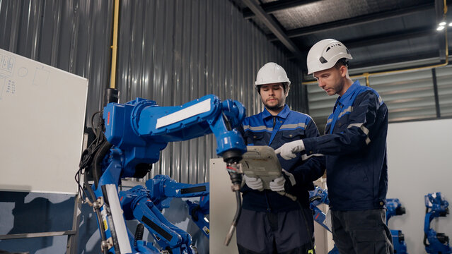 Robotics technician discuss robot programming and calibration beside robotic arm, supporting system integration. software setup, technical training safety, precision, reliability.
